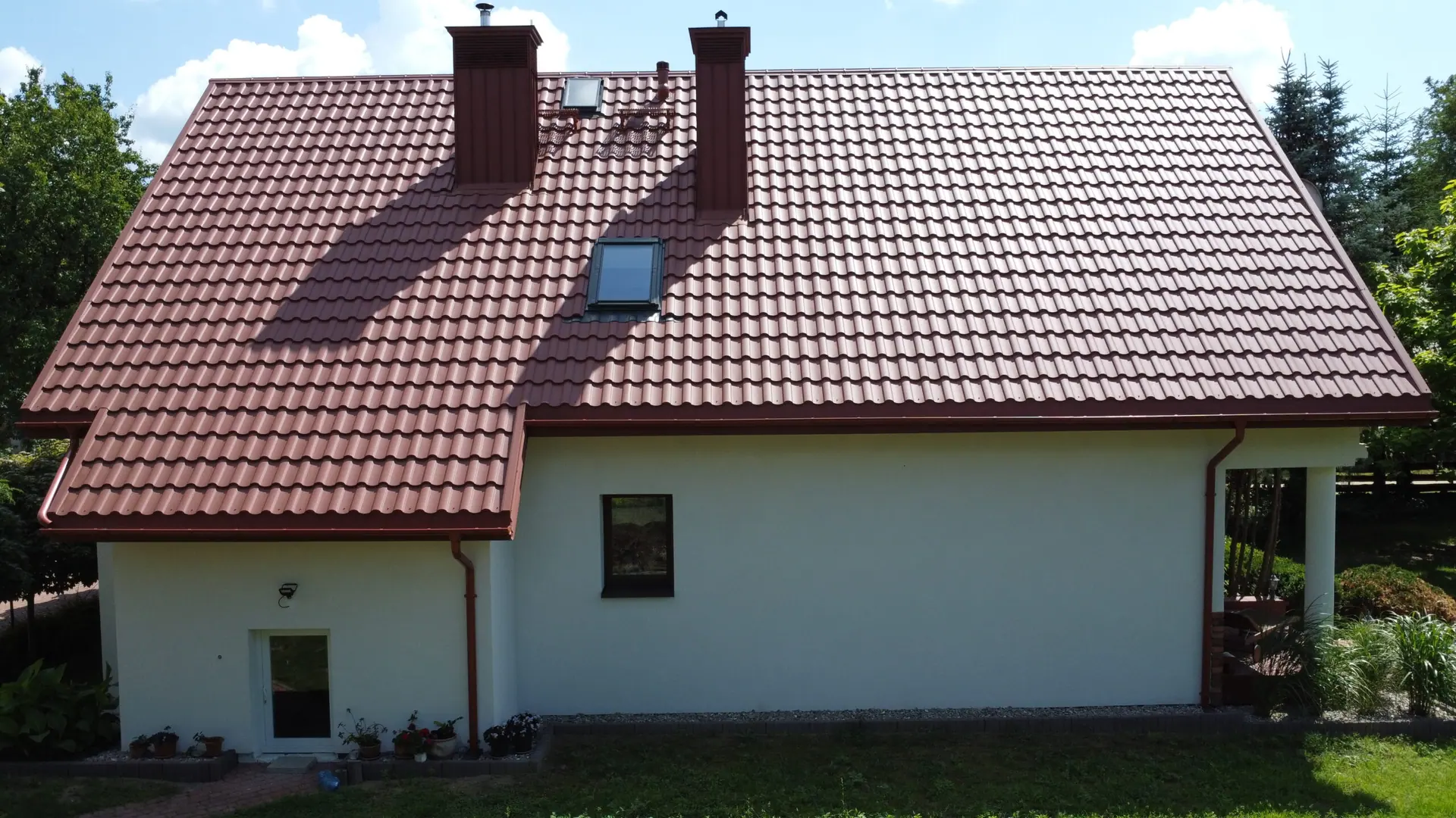 Czerwony dach dwuspadowy z kominem i oknem połaciowym