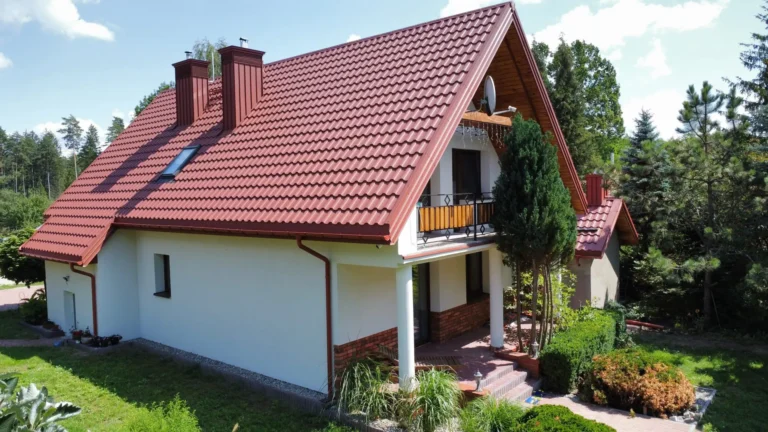 Czerwony dach domu z oknami połaciowymi widziany od ogrodu