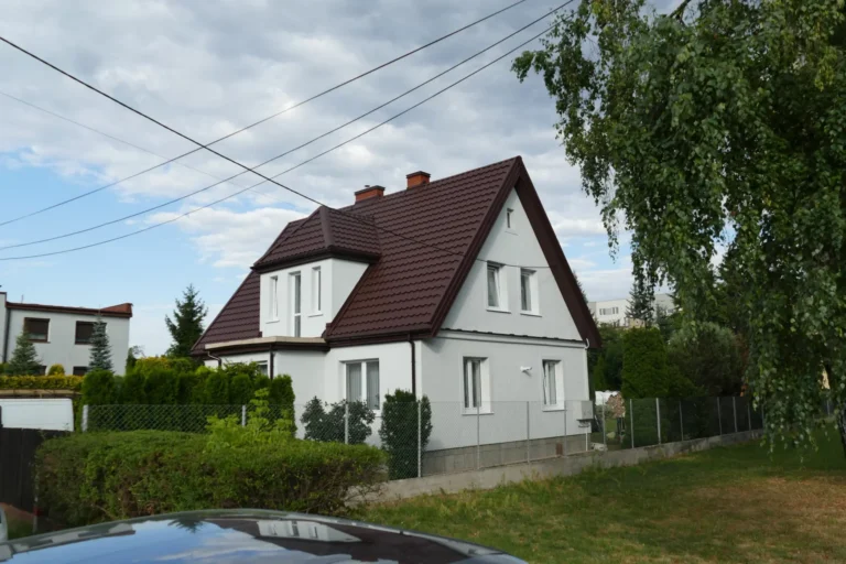 Dach domu z czerwonym pokryciem i jasną elewacją